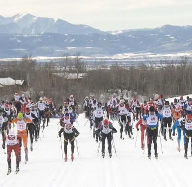 Cross-country skiers racing on a snowy trail with mountains in the background.