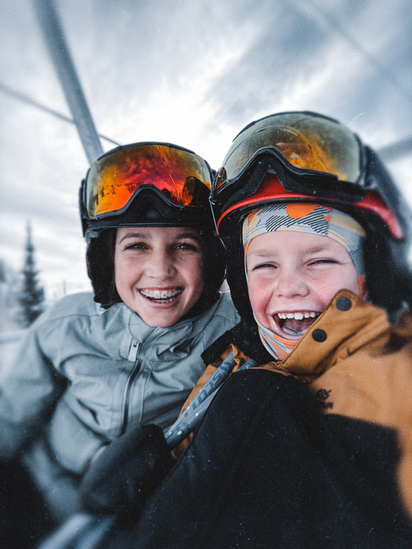 Two children in ski gear smiling on a snowy day.