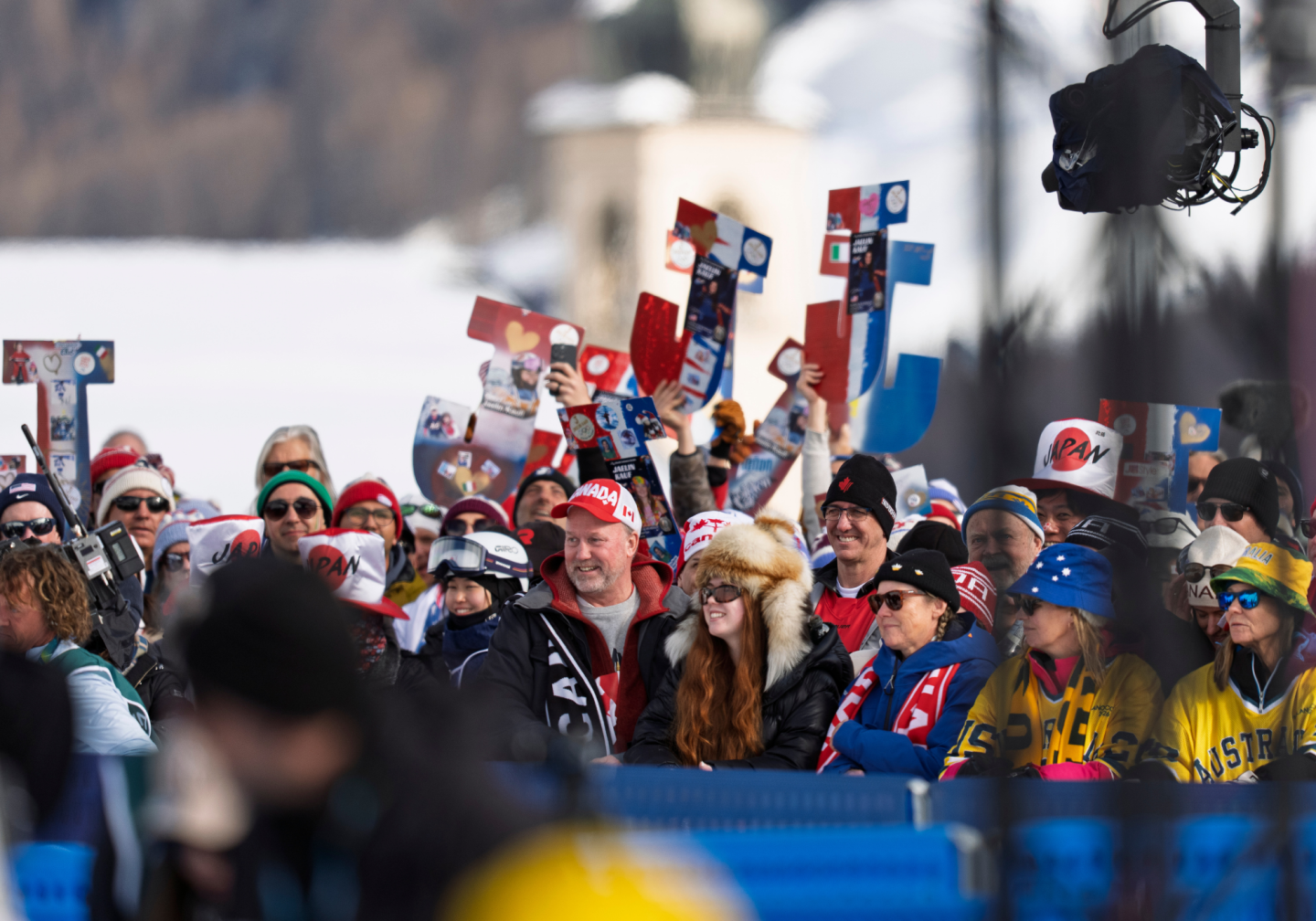 Crowd of cheering fans in winter clothing at a snowy outdoor event.