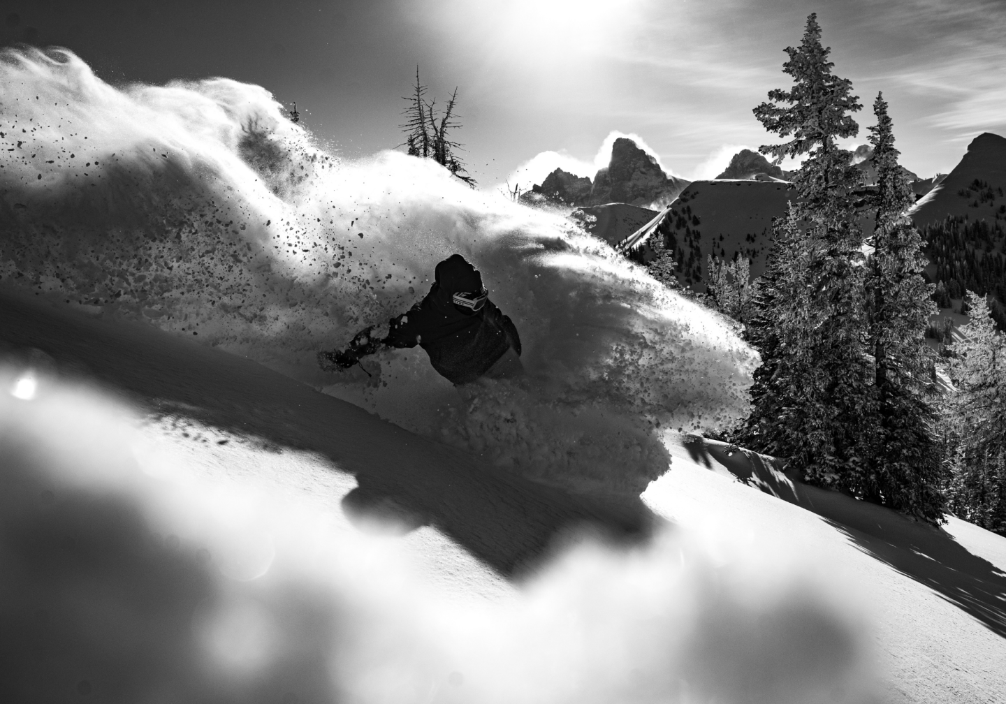Snowboarder carving through fresh powder in a mountainous landscape, black and white photo.