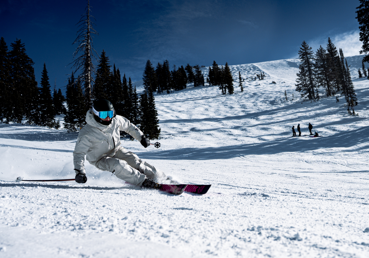 Skier in white suit carving down a snowy slope under a clear blue sky.