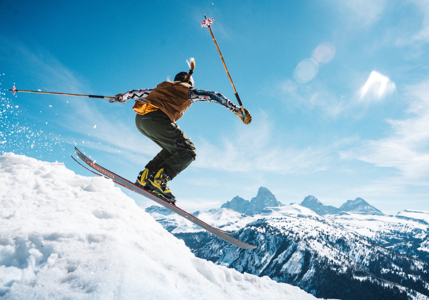 Skier jumping off snowy slope against a mountain backdrop.