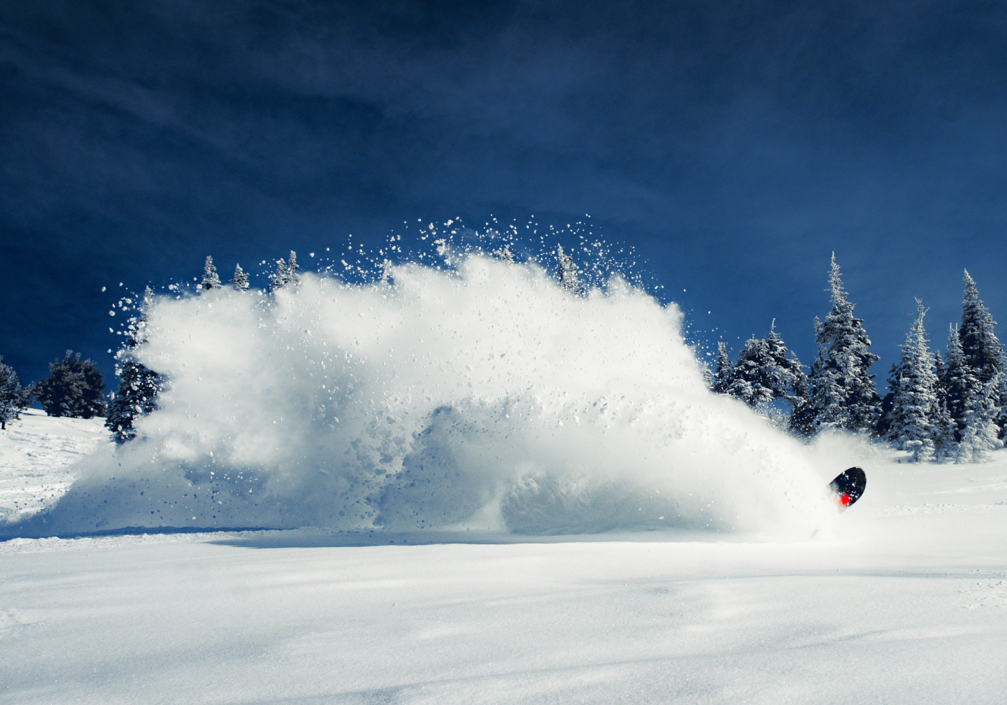 Snowboarder cutting through fresh powder under blue sky.