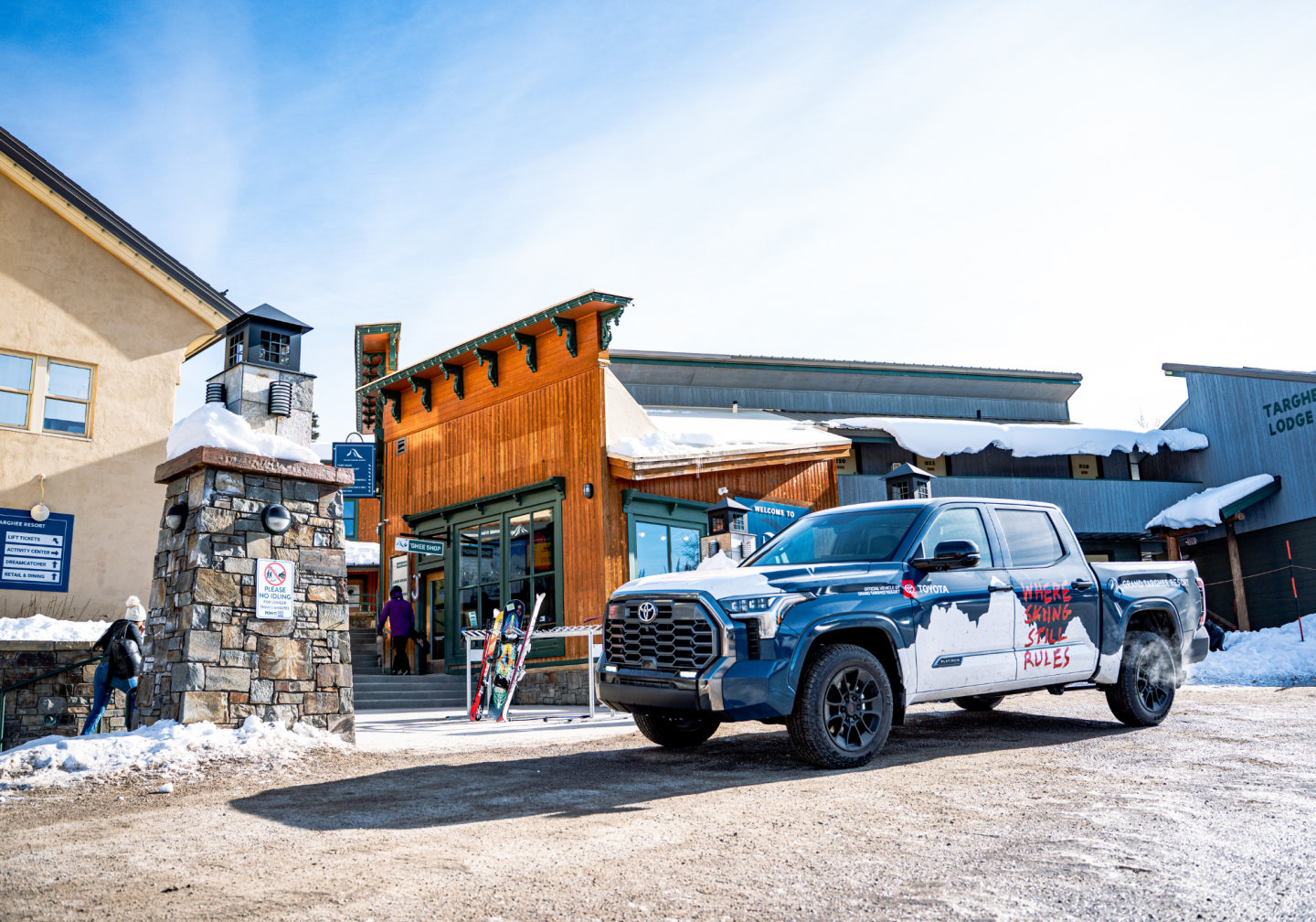Truck parked outside a snowy ski lodge on a bright day.