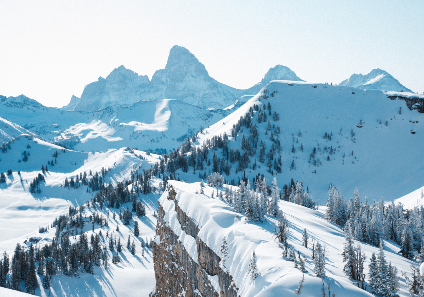 Snow-covered mountains with trees and clear blue sky.