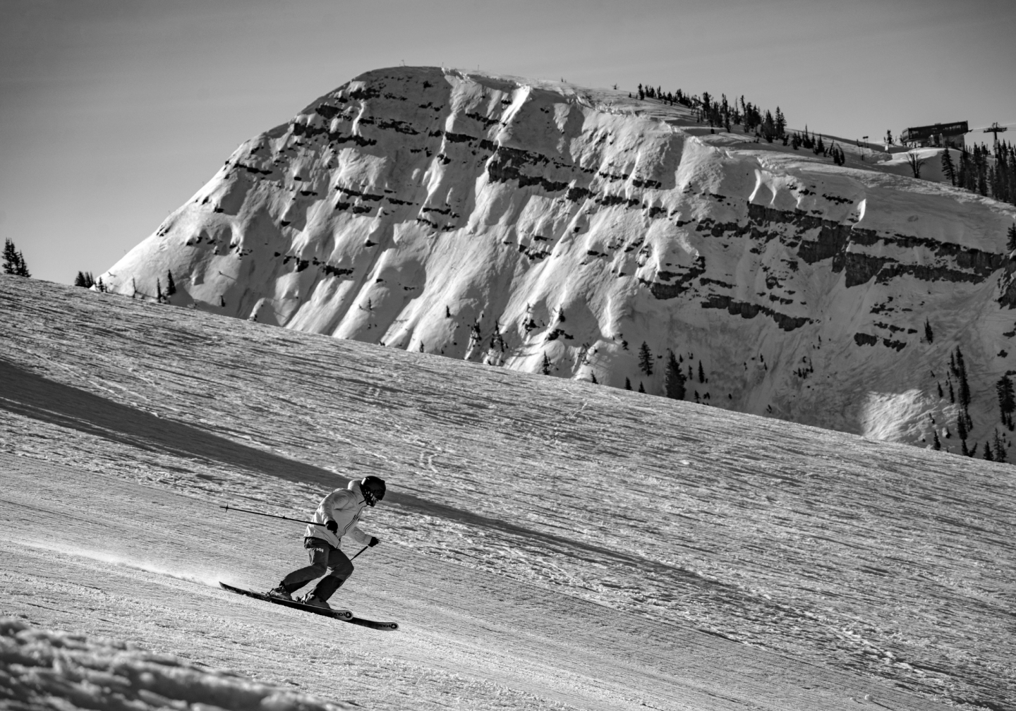 Skier racing downhill on a snowy slope, mountain in the background.