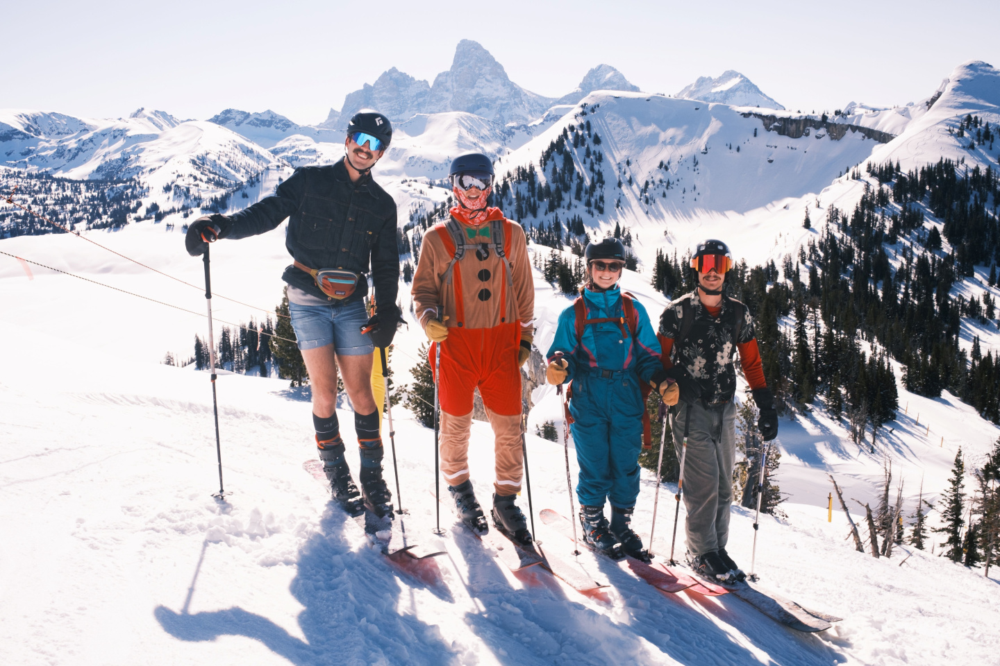 Four skiers in colorful outfits pose on a snowy mountain with clear skies.