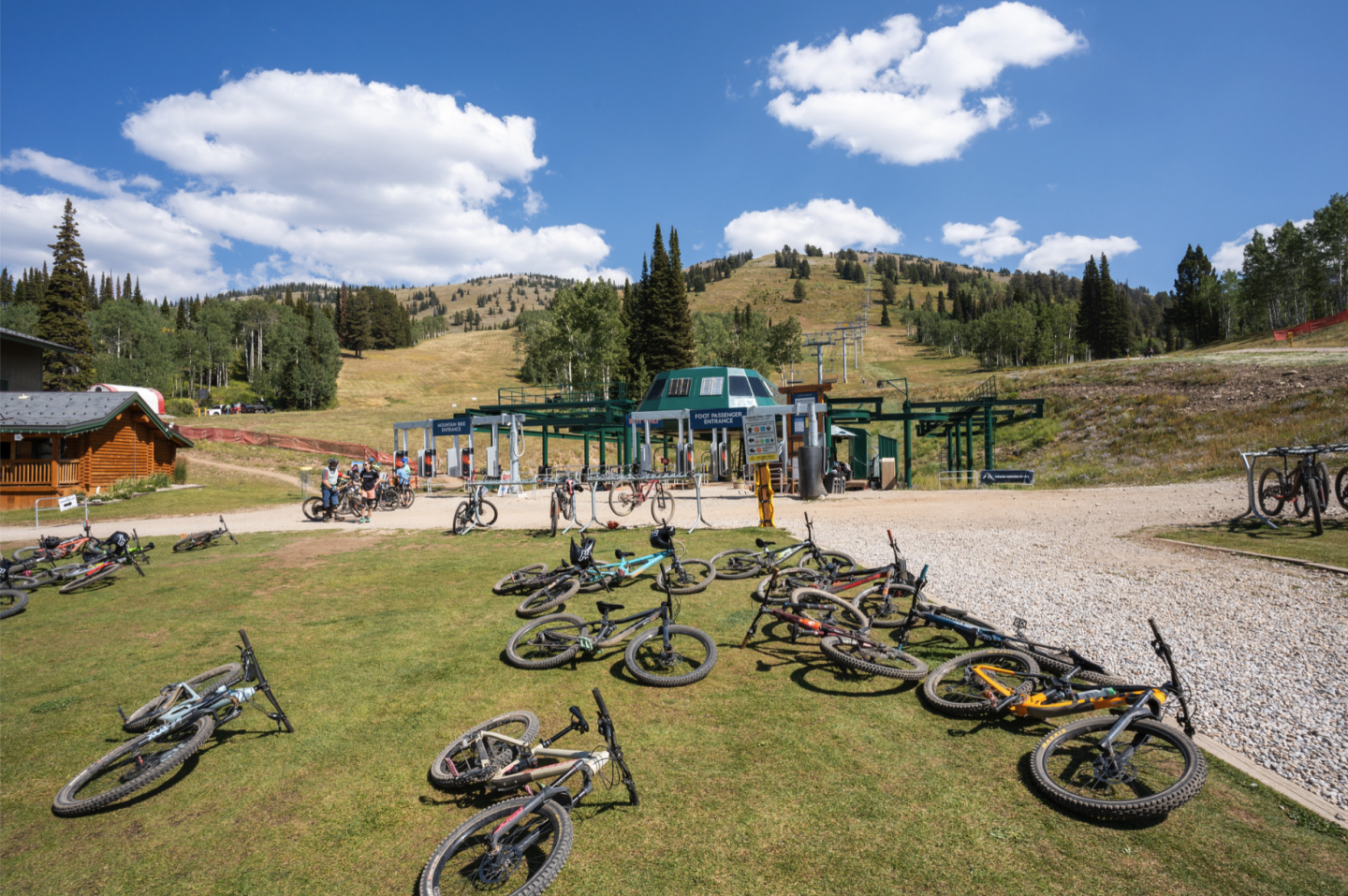 Bicycles scattered on grass at a mountain lift station under a blue sky.