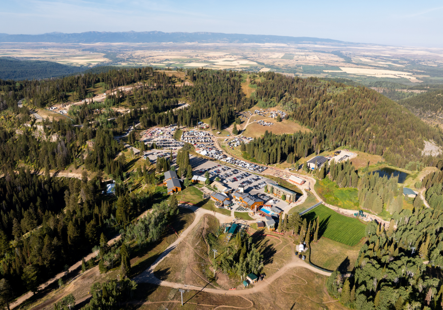 Aerial view of a forested village with winding roads and distant mountains.