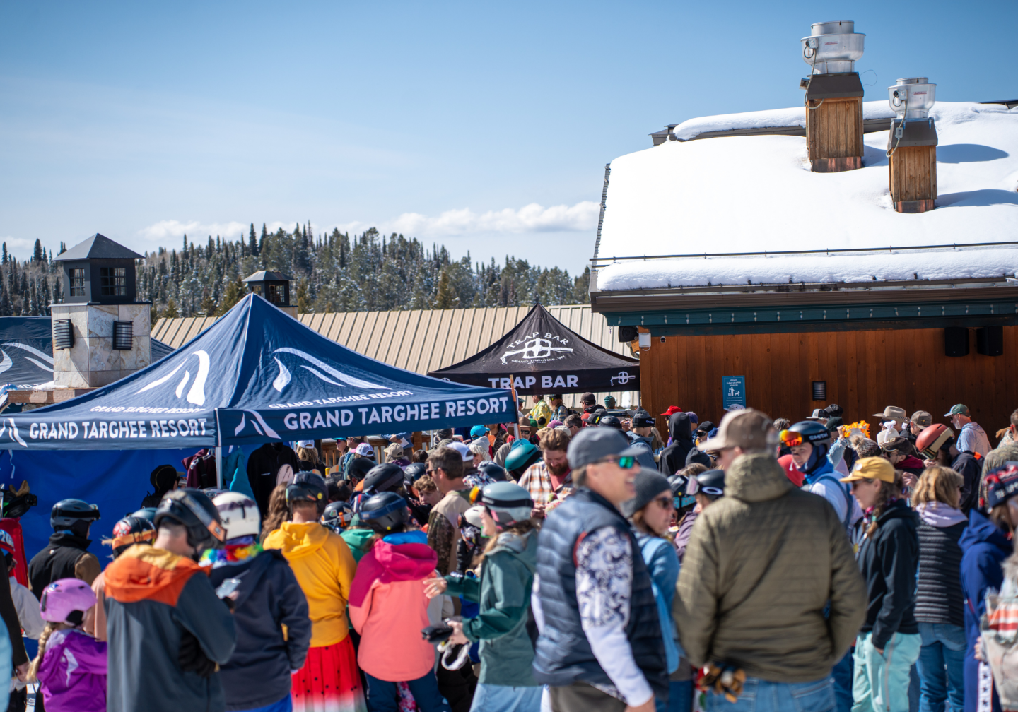 Crowd gathered at a snowy ski resort under clear blue skies.