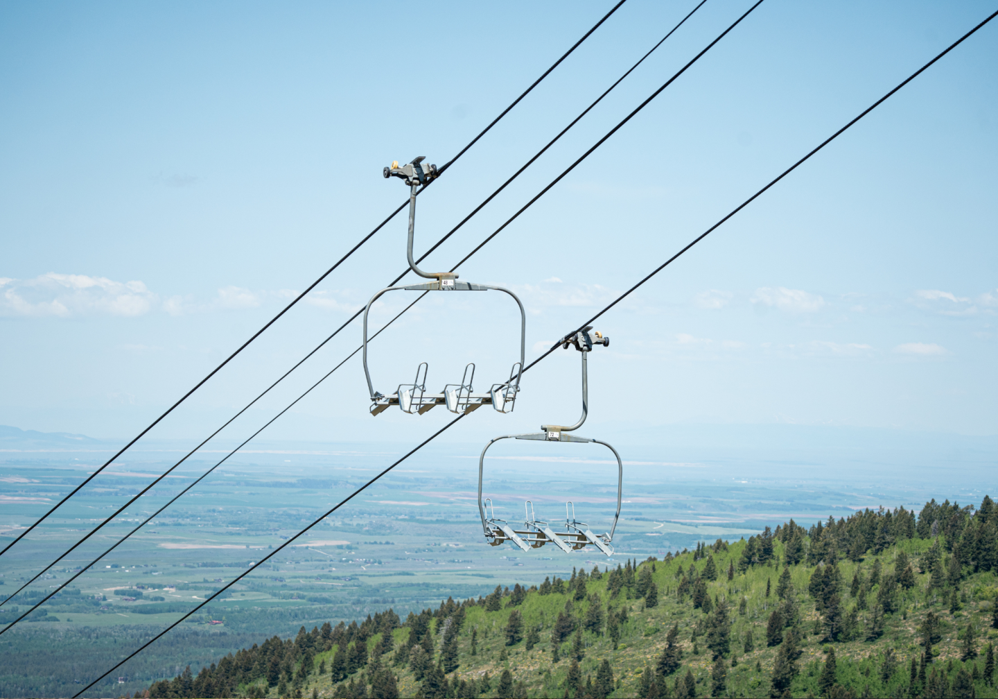 Chairlift ascending over green mountains against clear blue sky.