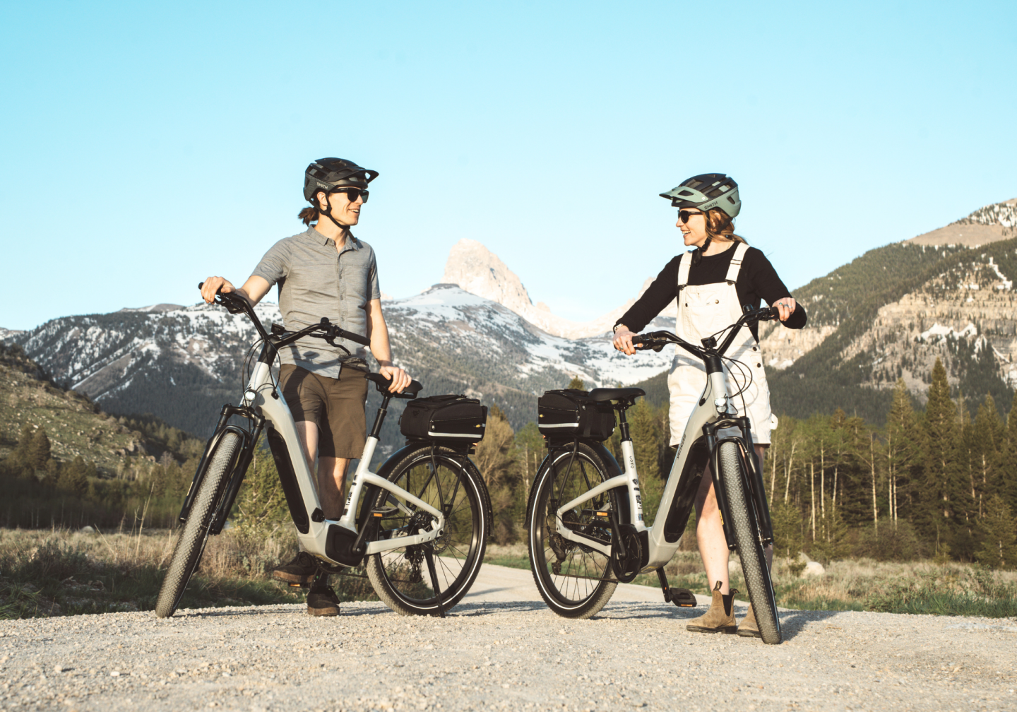 Two people with bikes in a scenic mountain setting, wearing helmets.