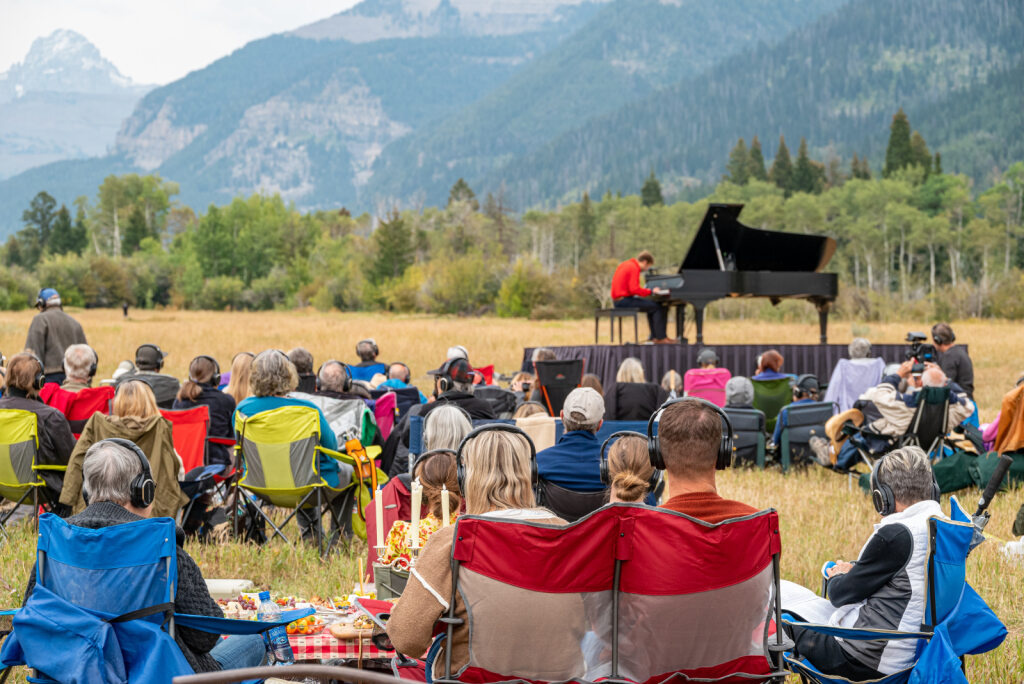 Outdoor piano concert in a field, audience seated on chairs.