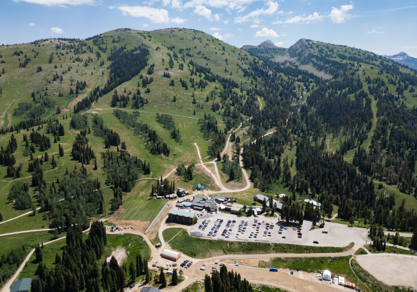 Mountain resort with parking lot surrounded by green hills and trees.