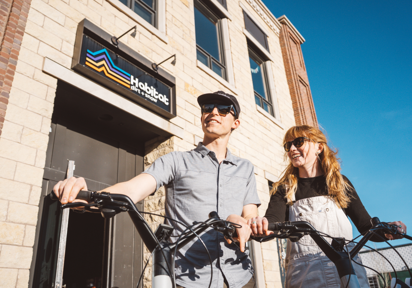 Two people with bikes outside a building under a clear blue sky.