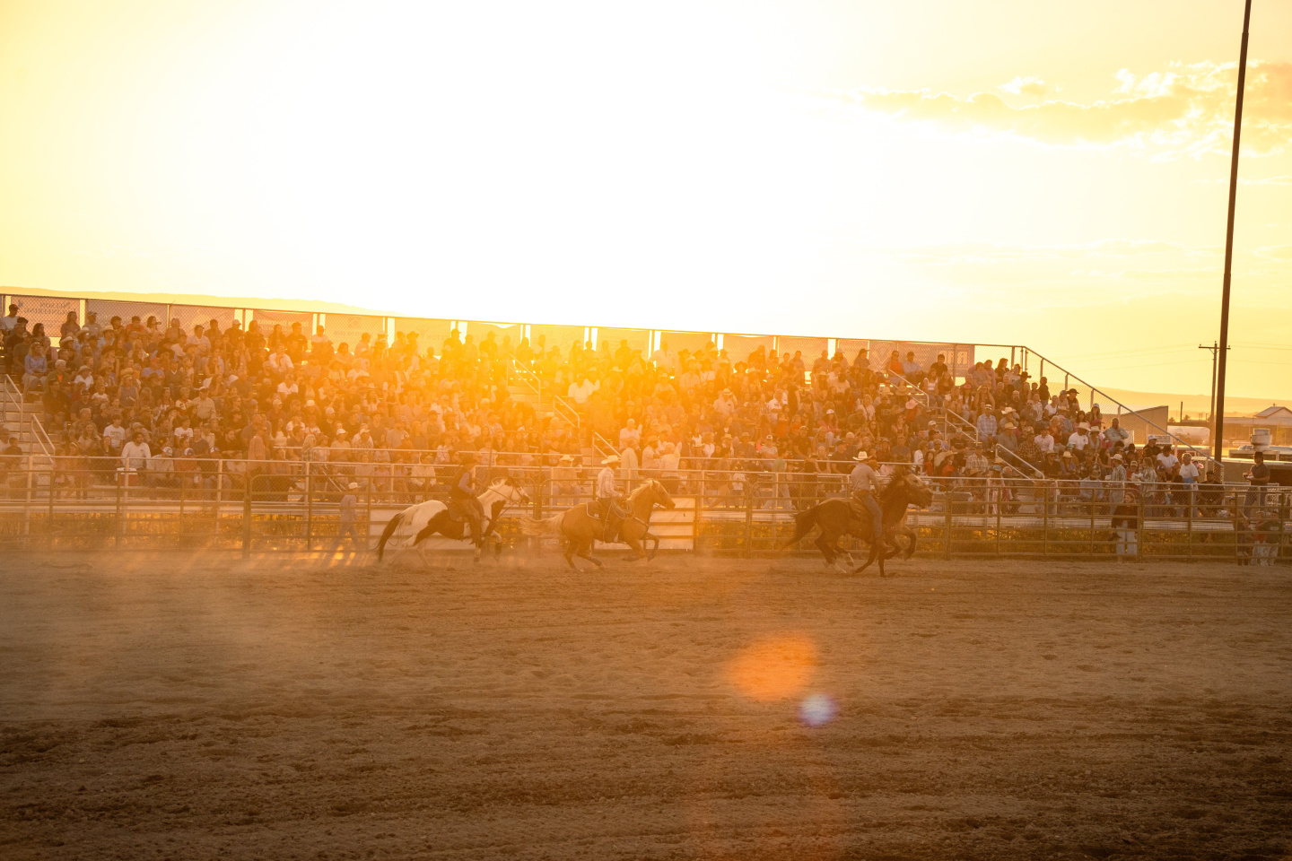 Rodeo at sunset with dust and a crowd in the stands.