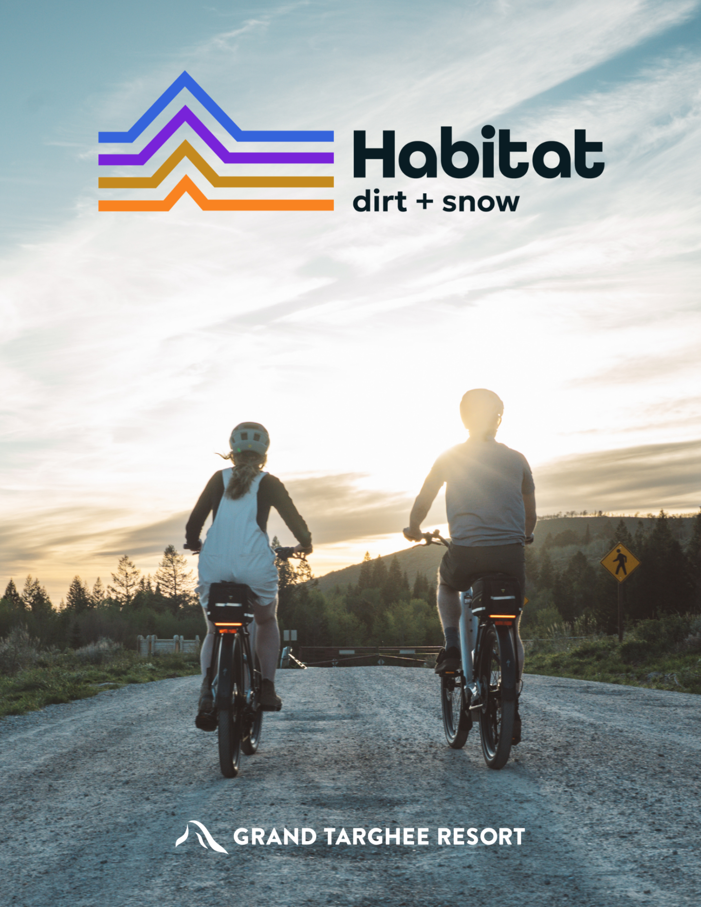 Two people biking on a dirt path at sunset, mountains in background.