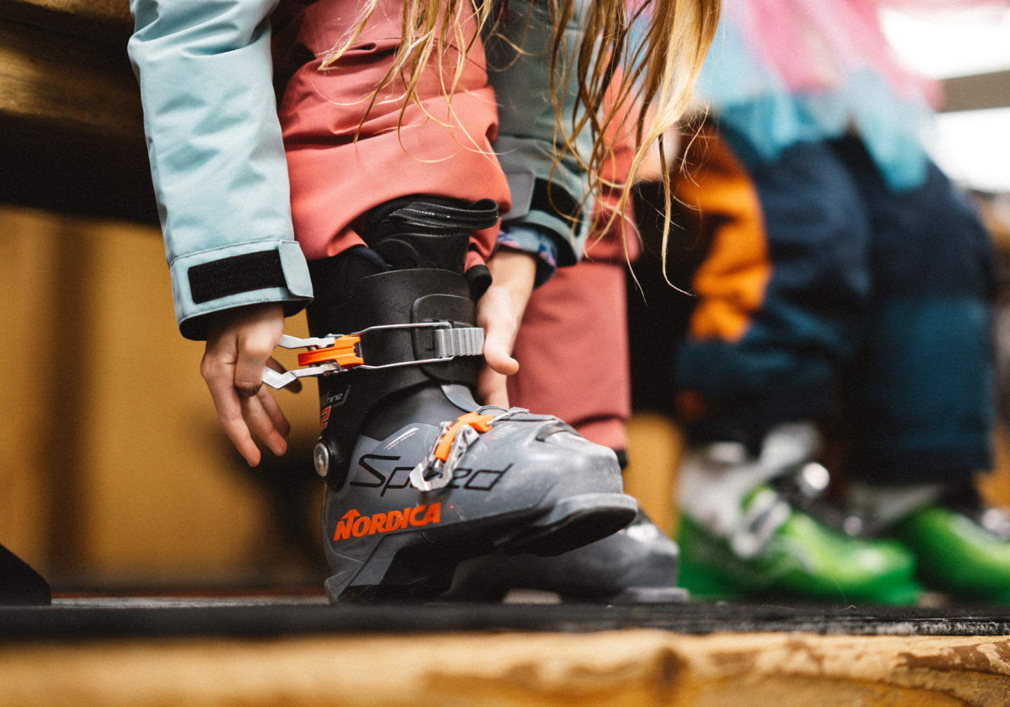 Child fastening a roller skate, with another skater blurred behind.