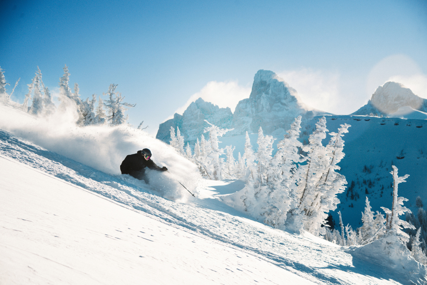 Skier carving through powder on a snowy mountain slope beneath blue skies