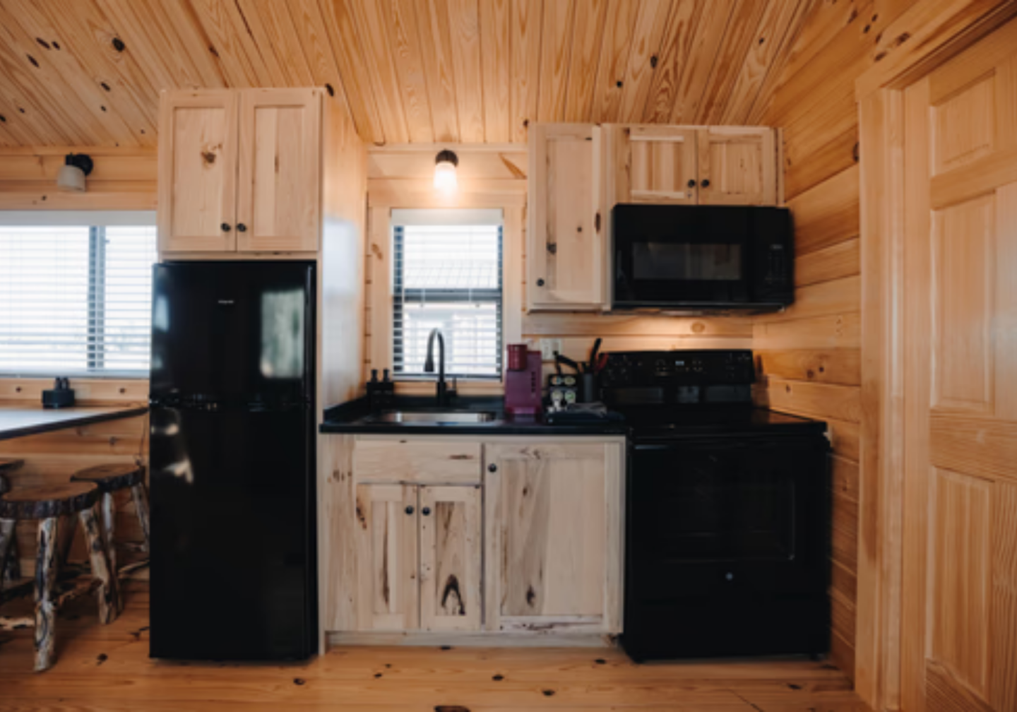 Cozy wood-paneled kitchen with black appliances and rustic cabinets.