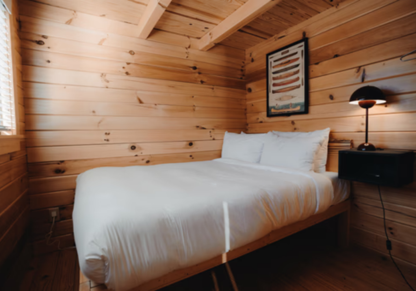 Cozy wooden cabin bedroom with a white bed and black bedside lamp.