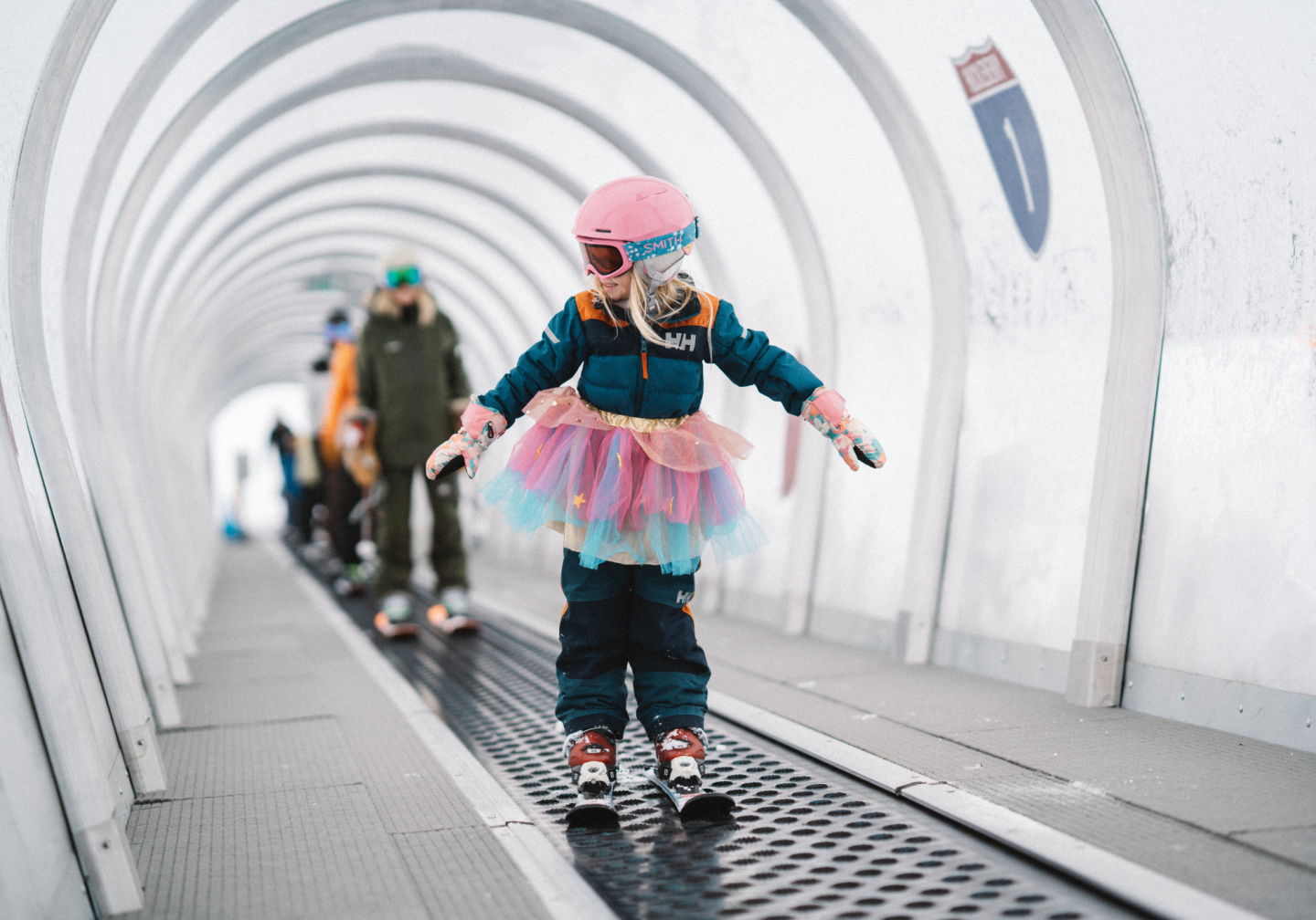 Child in a colorful tutu roller skating through a curved tunnel.