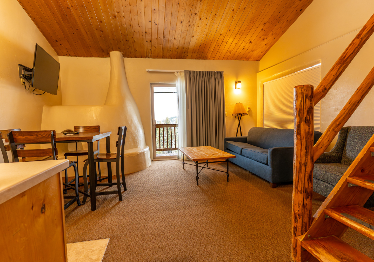 Cozy attic living room with wooden ceiling, blue sofa, dining table, and staircase