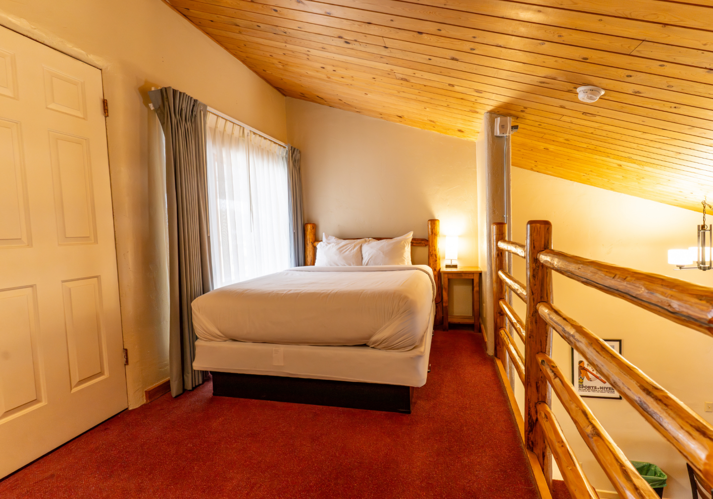 Cozy loft bedroom with white bed, red carpet, and wooden railing